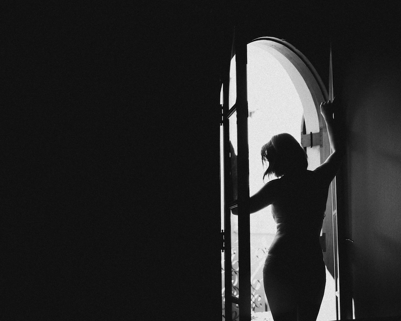 Silhueta de uma mulher abrindo uma porta, com a luz que vem de fora contornando seu corpo.