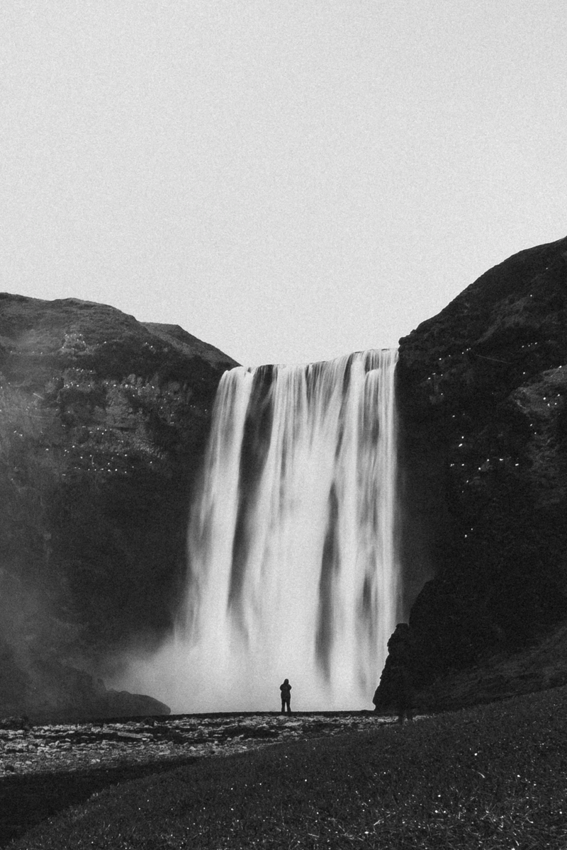 Foto de uma grande cachoeira aveludada, com uma pessoa bem pequena na parte inferior observando a água.