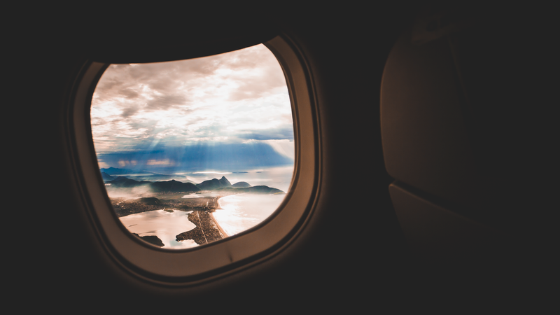 Foto de uma janelinha de avião com a paisagem montanhosa da região dos lagos, no RJ.
