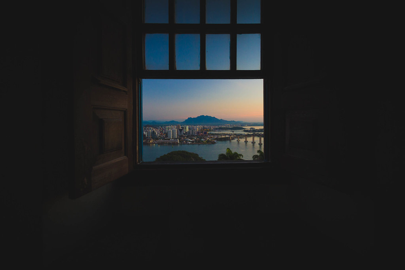 Foto da paisagem com mar e montanhas de Vila Velha vista através de uma janela do convento da Penha.