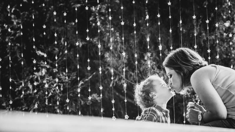 Foto em que uma criança pequena e sua mãe aparecem no canto direito do quadro dando um selinho.
