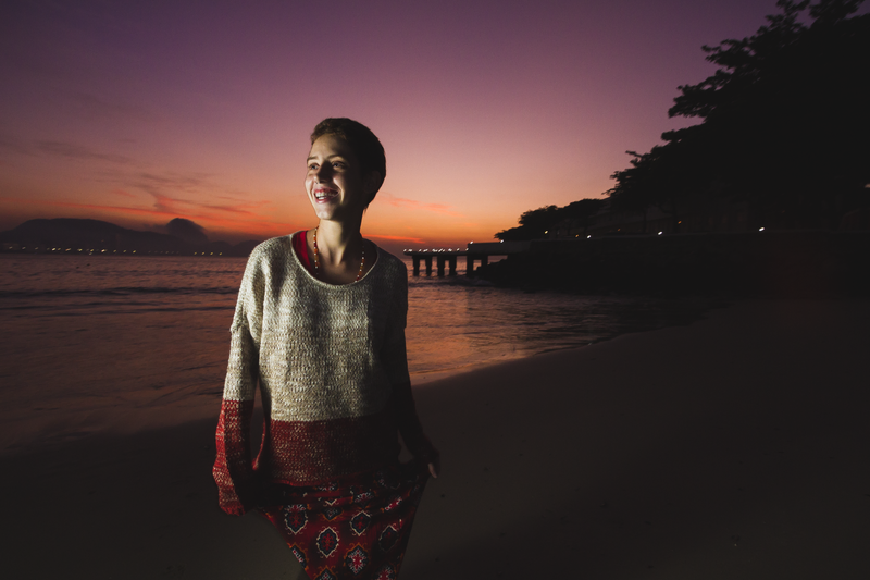 Foto da mulher na praia, desta vez iluminada com o flash – se vê tanto o céu em alvorada quanto os detalhes da modelo.
