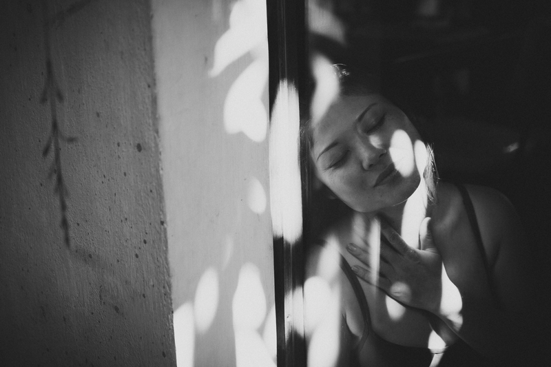 Retrato de mulher se apoiando em uma parede com a sombra de folhas fazendo texturas no rosto dela.