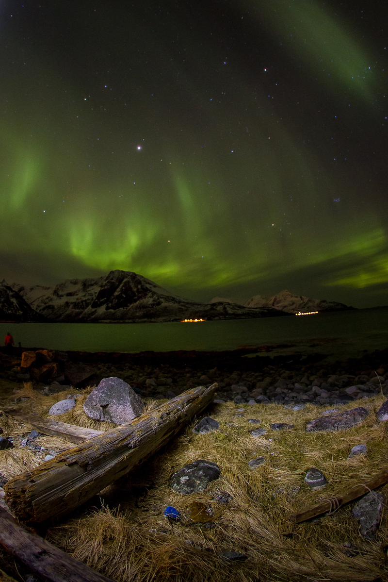Foto de um céu iluminado pela Aurora Boreal, montanhas, lagos e pedras na paisagem.
