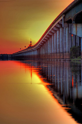 Foto de uma ponte com destaque para o rio e manchas avermelhadas nas bordas das mudanças de iluminação.