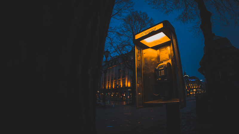 Imagem noturna de um telefone público com uma luz amarelada dentro dele.